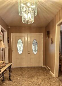Entrance doors view from inside white double door with oval glass inserts with crystal chandelier above